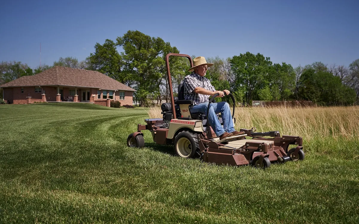 Riding mower cutting a large lawn around a rural home with open ground behind it